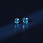 Sky blue topaz CZ round cushion stud earrings on dark navy surface - electric editorial style