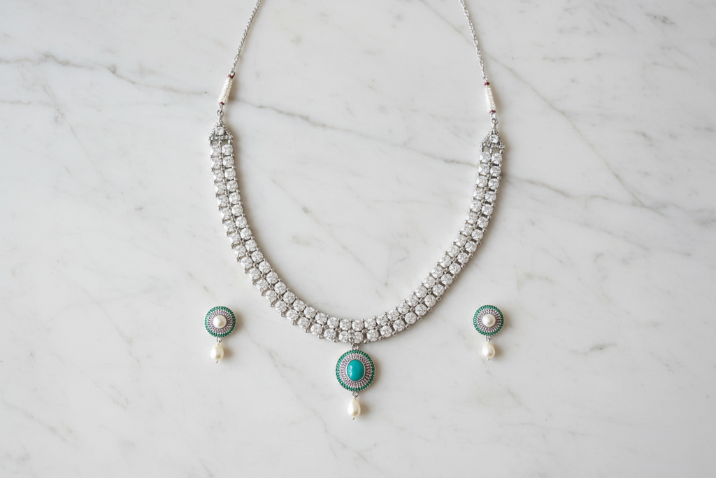 Flat lay of white AD necklace with teal pendant and pearl drop set on white marble