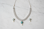 Flat lay of white AD necklace with teal pendant and pearl drop set on white marble