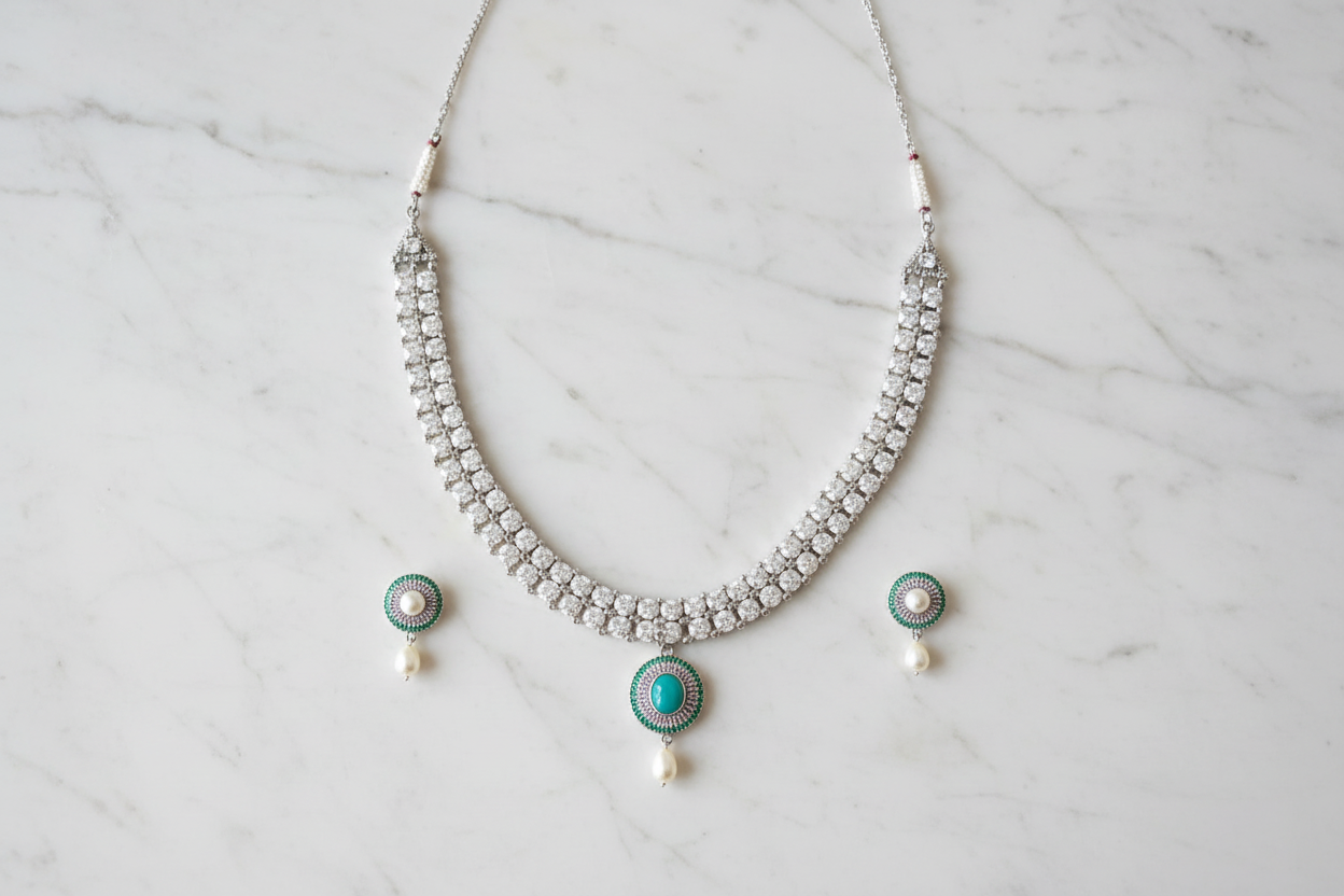 Flat lay of white AD necklace with teal pendant and pearl drop set on white marble