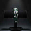 Emerald green baguette AD bangle with white floral AD sculpture on dark velvet studio display
