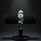 Emerald green baguette AD bangle with white floral AD sculpture on dark velvet studio display
