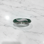 Flat lay top-down view of emerald baguette and white AD pavé wave bangle bracelet on white marble