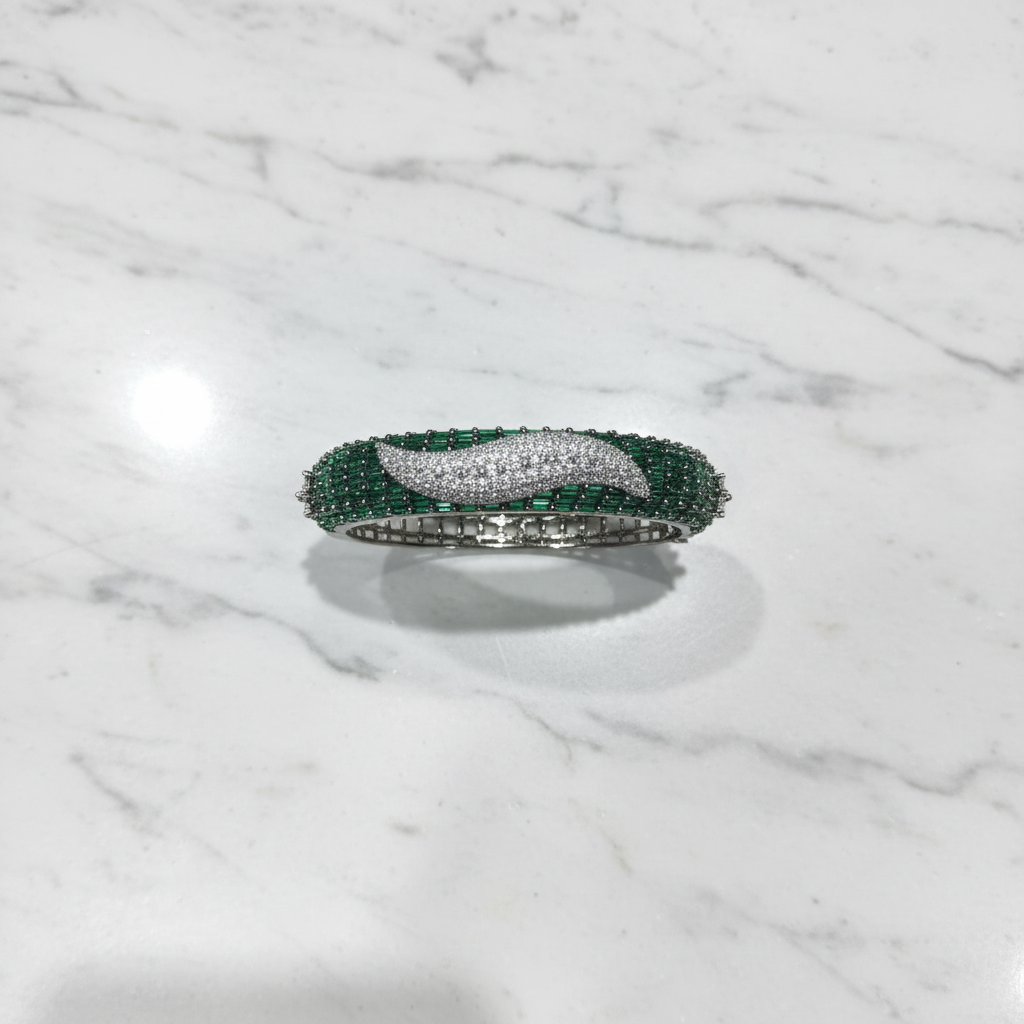 Flat lay top-down view of emerald baguette and white AD pavé wave bangle bracelet on white marble