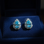 Aqua blue CZ teardrop halo stud earrings on navy velvet - dark editorial style