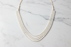 Flat lay of 4-strand layered white seed pearl necklace on white marble