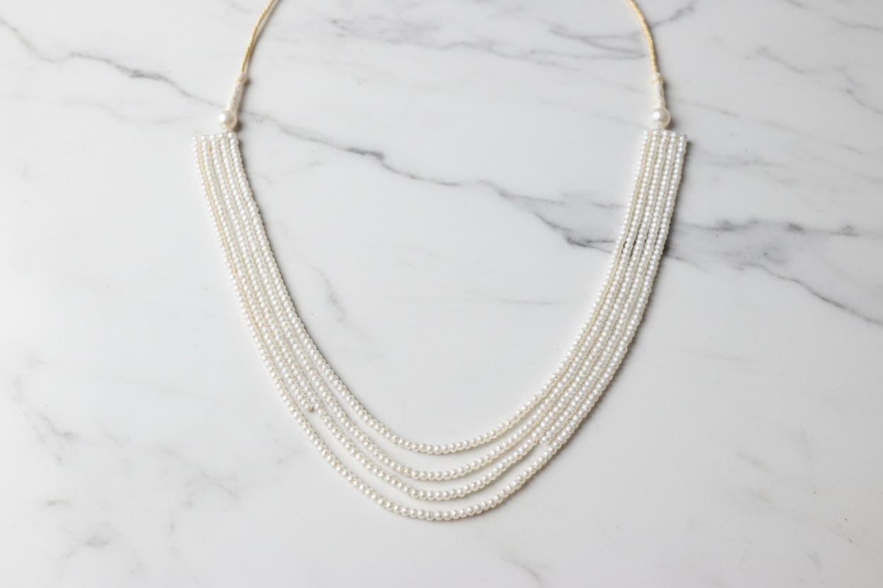 Flat lay of 4-strand layered white seed pearl necklace on white marble
