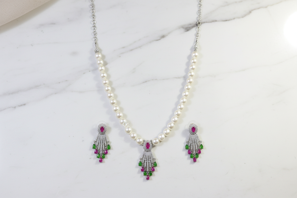 Flat lay of pearl necklace with ruby and green AD tassel pendant set on white marble