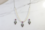 Flat lay of pearl necklace with ruby and green AD tassel pendant set on white marble