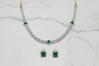 Flat lay of white AD tennis necklace with emerald stations and earrings on white marble