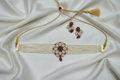 Multi-strand seed pearl choker with AD floral medallion and ruby emerald centre set — flat lay on ivory silk