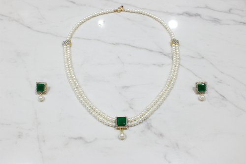 Flat lay of 2-strand seed pearl choker with emerald square AD pendant and earrings on white marble