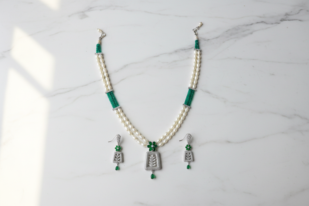 Flat lay of pearl and teal AD pendant necklace set with earrings on white marble