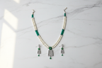 Flat lay of pearl and teal AD pendant necklace set with earrings on white marble