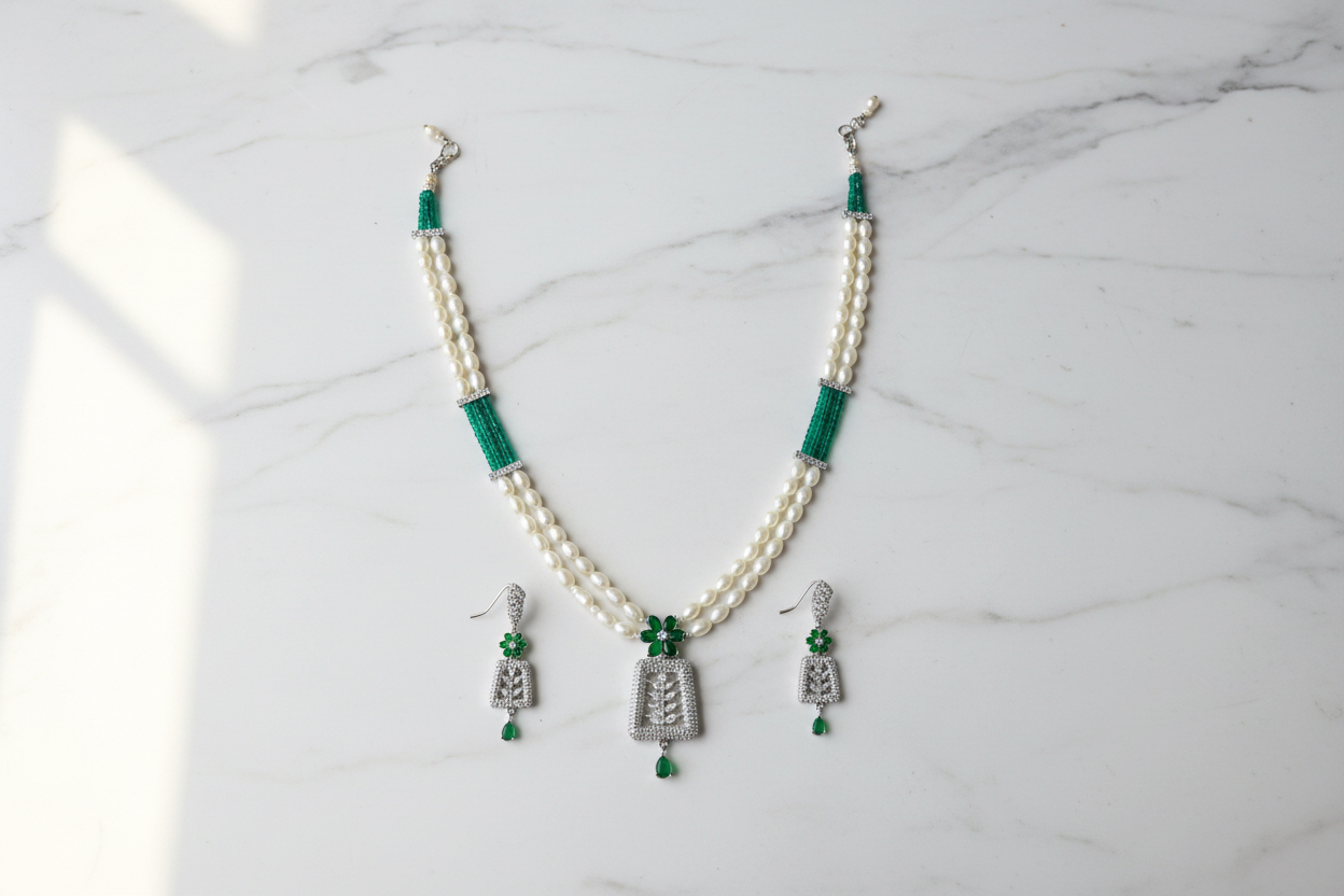 Flat lay of pearl and teal AD pendant necklace set with earrings on white marble