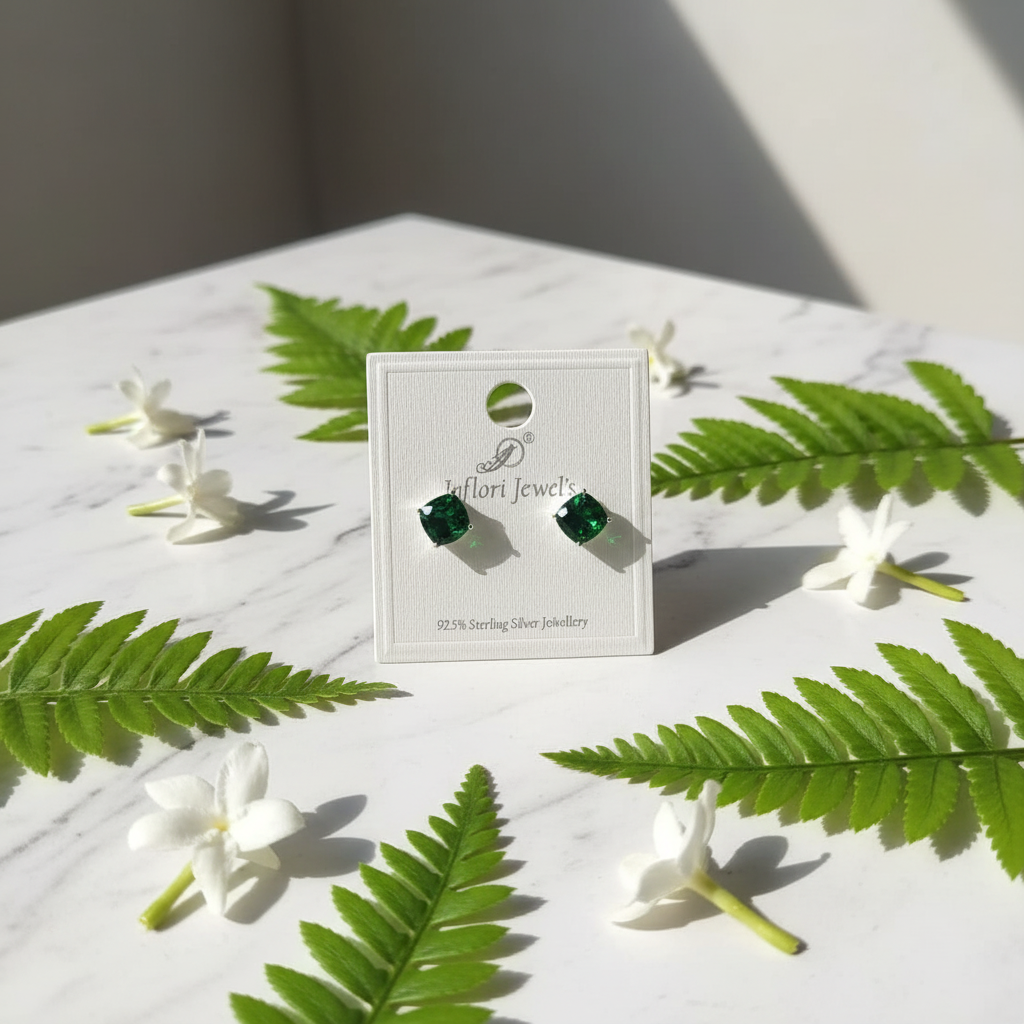 Emerald green CZ cushion square solitaire stud earrings on white marble with fern and jasmine - lifestyle style
