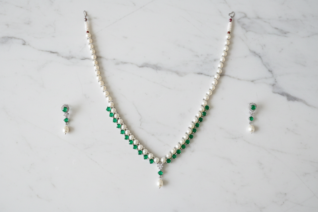 Flat lay of pearl and emerald green AD necklace set with earrings on white marble