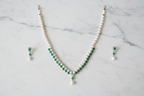 Flat lay of pearl and emerald green AD necklace set with earrings on white marble