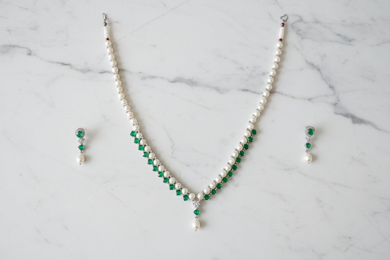 Flat lay of pearl and emerald green AD necklace set with earrings on white marble