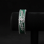 Emerald green baguette AD bangle with white marquise leaf overlay on dark velvet studio display