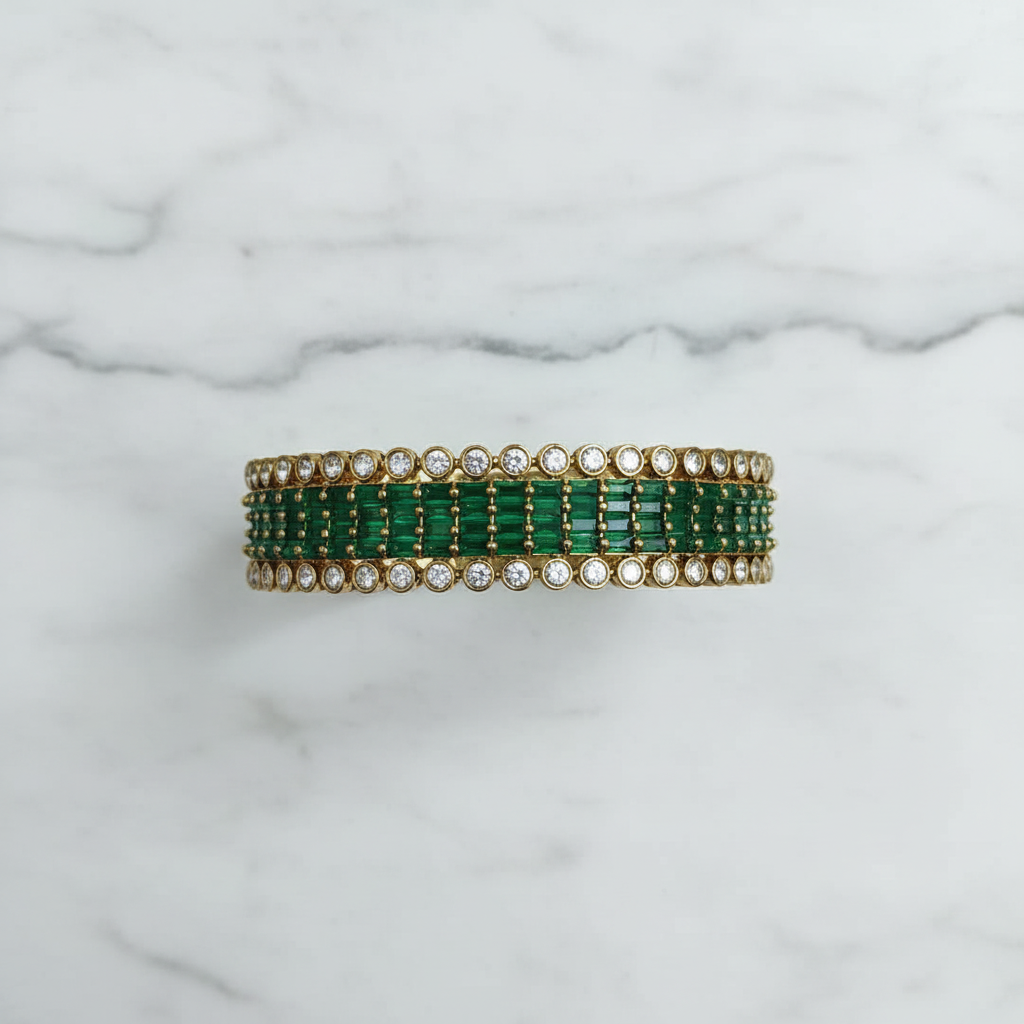 Flat lay top-down view of emerald green baguette AD bangle with round polki AD border in gold tone on white marble