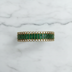 Flat lay top-down view of emerald green baguette AD bangle with round polki AD border in gold tone on white marble