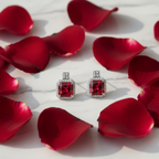 Ruby red CZ cushion halo drop earrings on white marble with rose petals - romantic lifestyle style