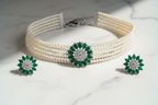 Flat lay of 3-strand seed pearl choker with emerald floral AD centrepiece and earrings on white marble