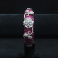 Ruby pink baguette AD bangle with white floral AD sculpture on dark velvet studio display