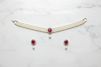 Flat lay of 2-strand seed pearl choker with ruby oval AD pendant and earrings on white marble