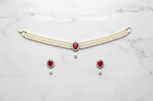 Flat lay of 2-strand seed pearl choker with ruby oval AD pendant and earrings on white marble