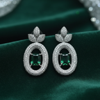 Emerald solitaire drop earrings on forest green velvet editorial flat lay