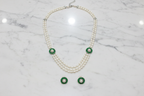 Flat lay of 3-strand pearl long necklace with emerald floral AD stations and earrings on white marble