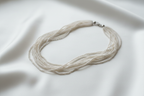 Flat lay of white seed bead necklace on white silk