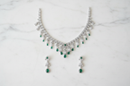 Emerald and diamond AD fringe necklace set flat lay on white marble