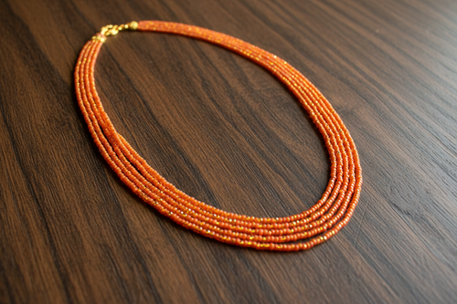Flat lay of orange and gold seed bead necklace on dark wood surface