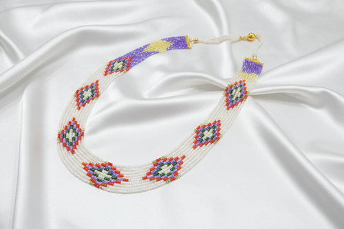 Flat lay of white and multicolor seed bead necklace on white silk