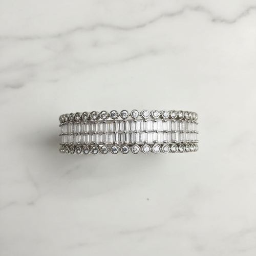 Flat lay top-down view of all-white baguette AD bangle with round polki AD border on white marble