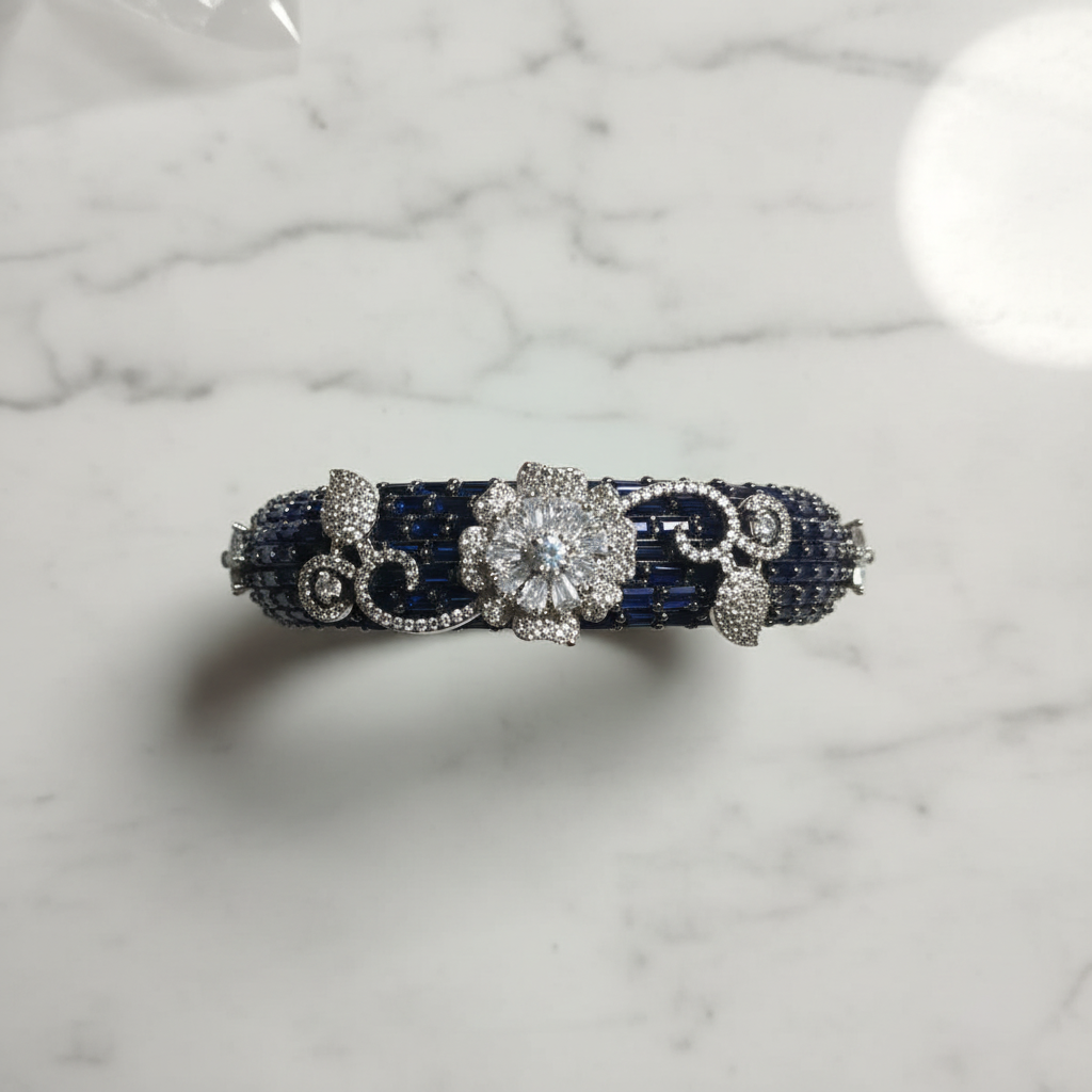 Flat lay top-down view of navy blue sapphire baguette AD bangle with white floral AD sculpture on white marble