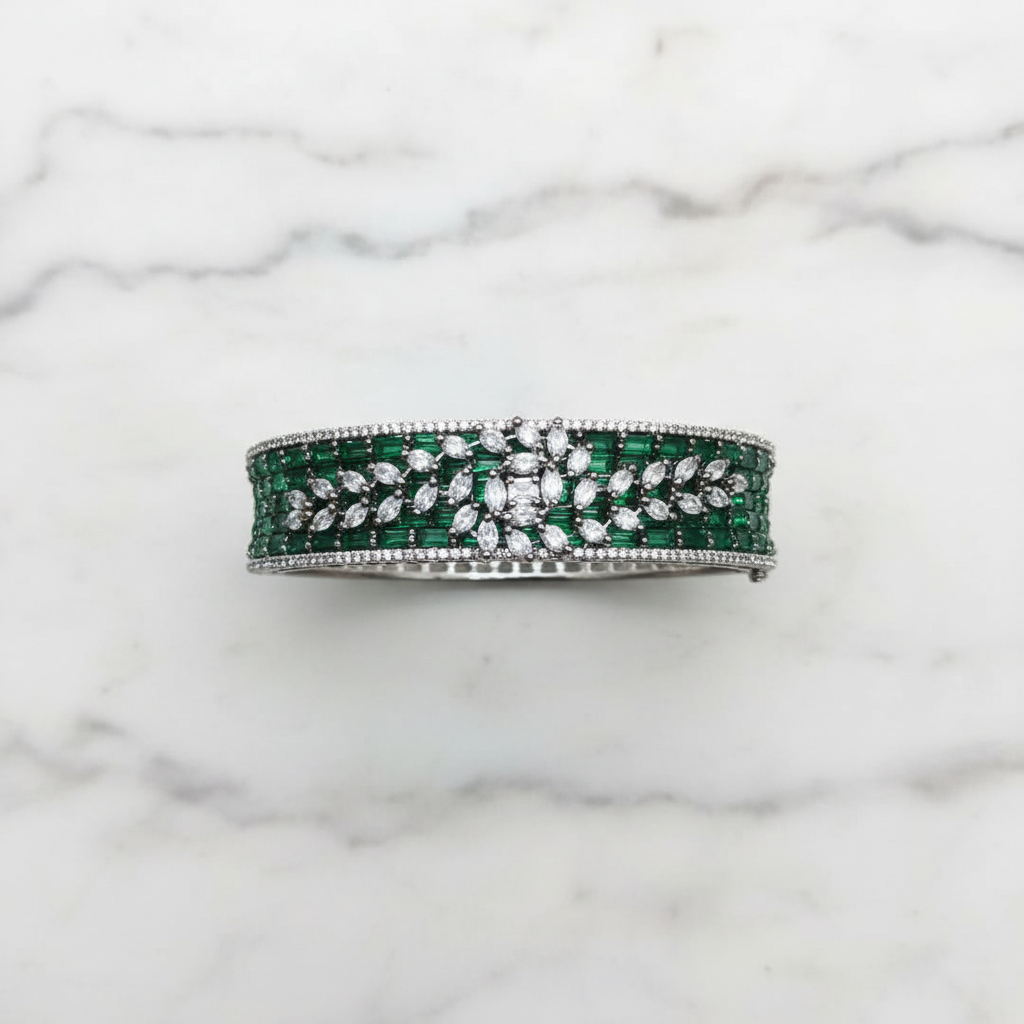 Flat lay top-down view of emerald green baguette AD bangle with white marquise leaf overlay on white marble