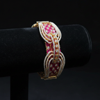 Ruby pink open-work AD bangle with gold tone arch lattice design on dark velvet studio display
