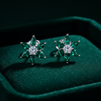 Emerald green CZ floral star stud earrings on forest green velvet - dramatic editorial style