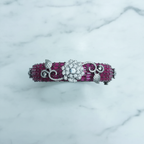 Flat lay top-down view of ruby pink baguette AD bangle with white floral AD sculpture on white marble