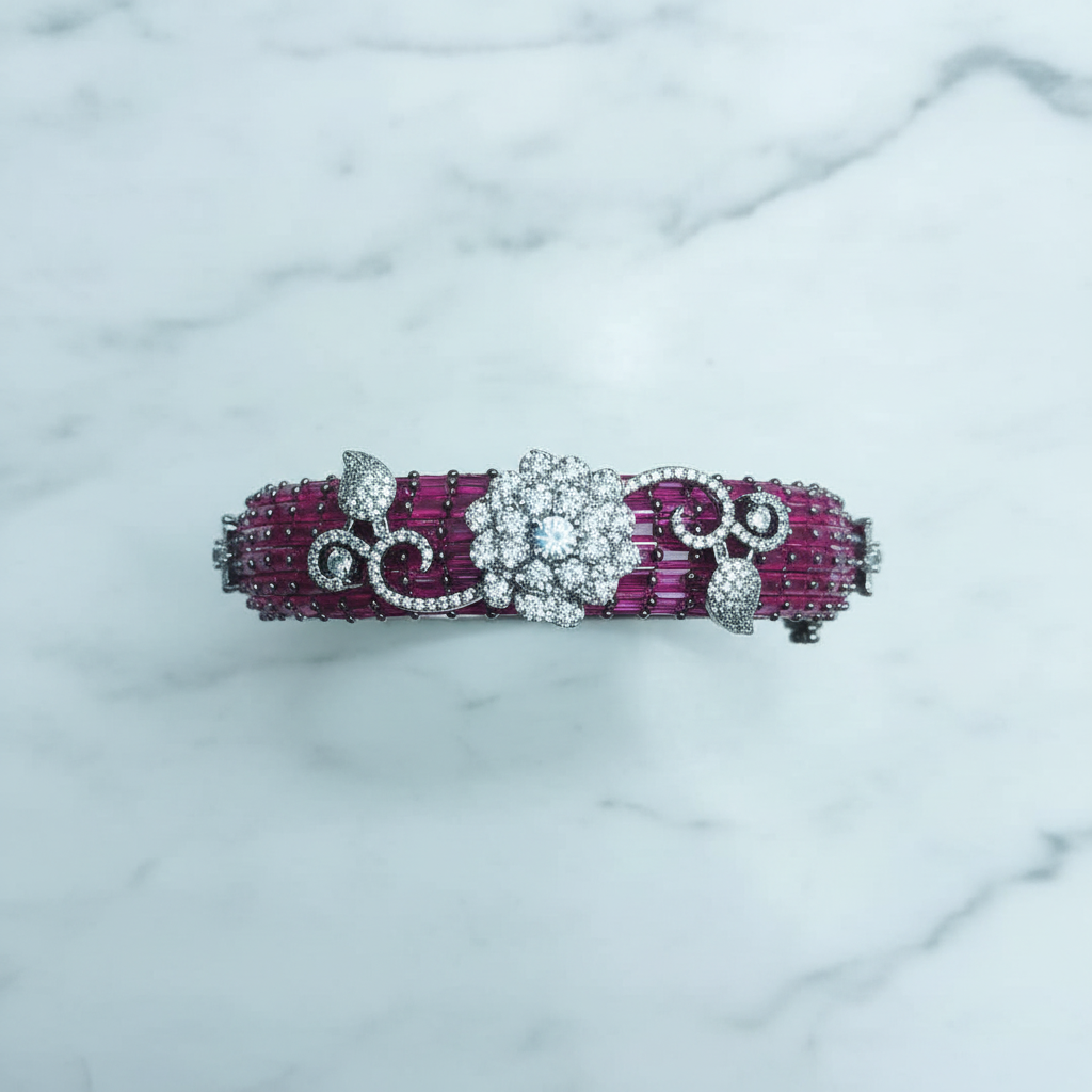 Flat lay top-down view of ruby pink baguette AD bangle with white floral AD sculpture on white marble