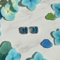 Aqua blue CZ cushion square halo stud earrings on white marble with hydrangea and sea glass - coastal lifestyle style