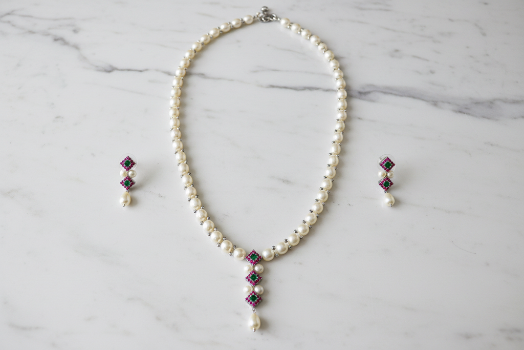 Flat lay of pearl and emerald AD floral pendant necklace set with earrings on white marble