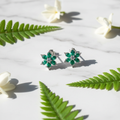 Emerald green CZ floral star stud earrings on white marble with fern and jasmine - garden lifestyle style