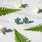 Emerald green CZ floral star stud earrings on white marble with fern and jasmine - garden lifestyle style