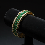 Emerald green baguette AD bangle with round polki AD border in gold tone on dark velvet studio display