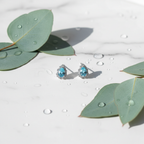 Aqua blue CZ teardrop halo stud earrings on white marble with eucalyptus - lifestyle style